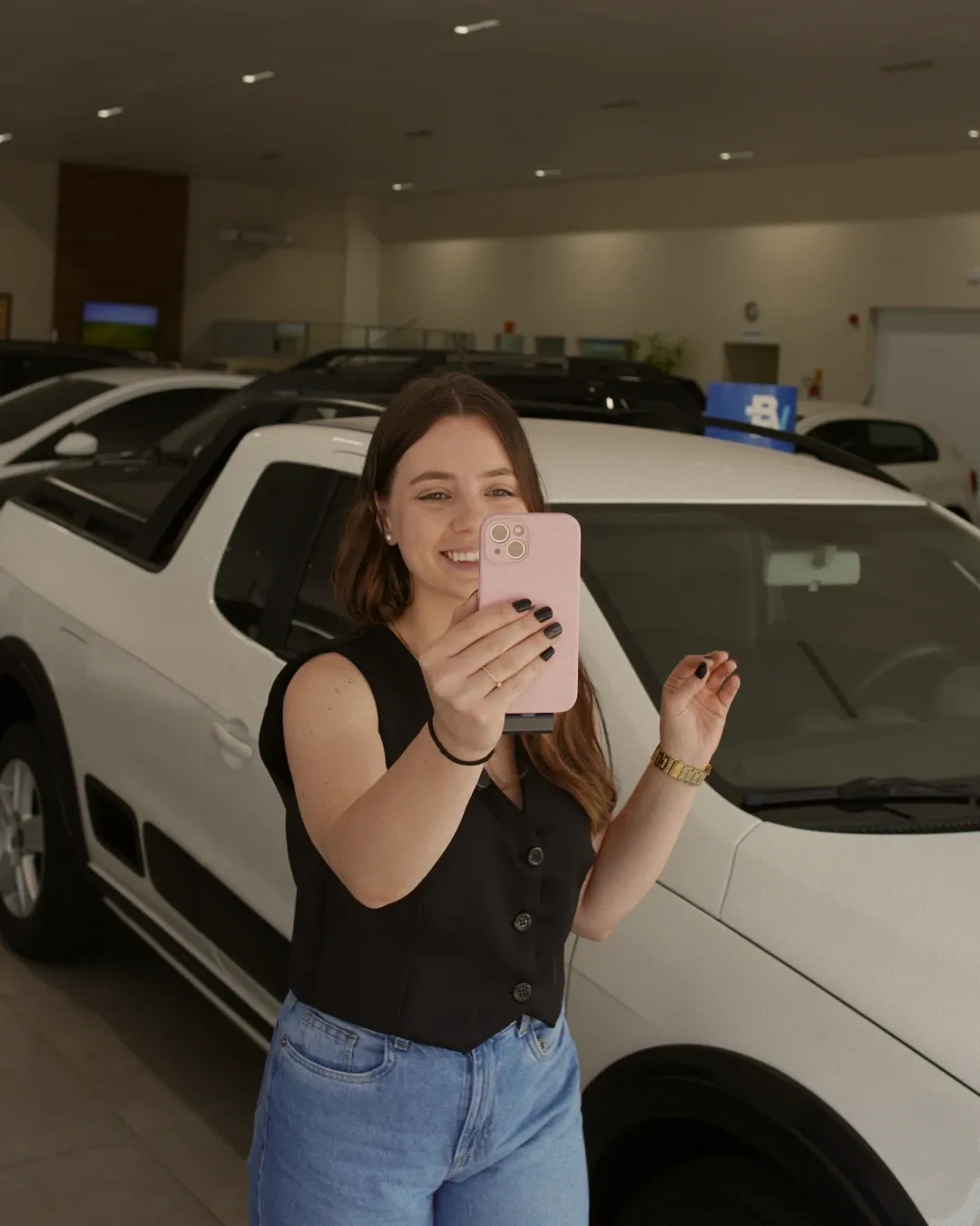 Mulher gravando um vídeo com o celular ao lado de uma picape branca no pátio de uma loja